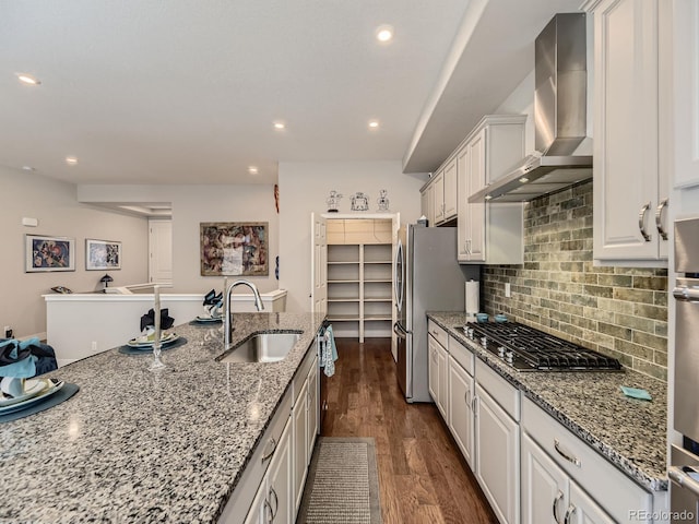 kitchen with dark wood finished floors, stainless steel appliances, decorative backsplash, a sink, and wall chimney range hood