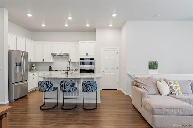 kitchen with a breakfast bar, appliances with stainless steel finishes, open floor plan, white cabinets, and under cabinet range hood