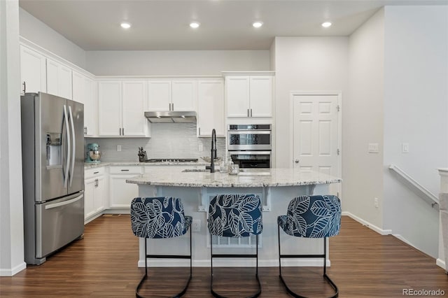 kitchen featuring stainless steel appliances, white cabinetry, under cabinet range hood, and a kitchen bar