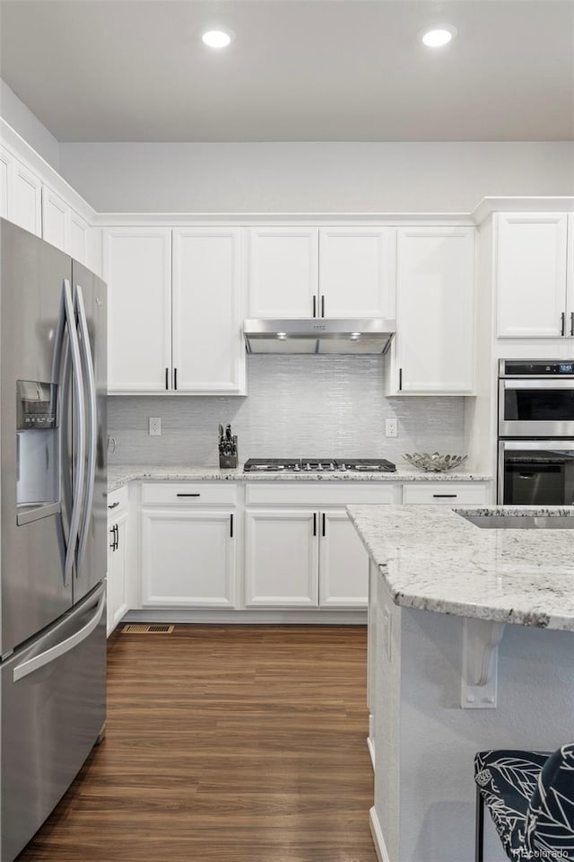 kitchen with white cabinets, decorative backsplash, dark wood-style floors, appliances with stainless steel finishes, and under cabinet range hood