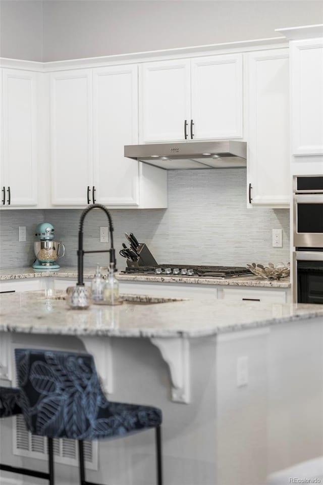 kitchen with stainless steel appliances, under cabinet range hood, white cabinets, and decorative backsplash