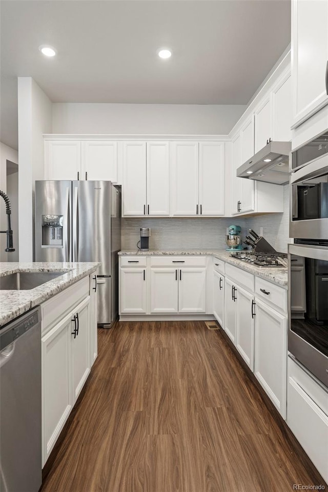 kitchen featuring white cabinets, appliances with stainless steel finishes, dark wood-style flooring, under cabinet range hood, and a sink