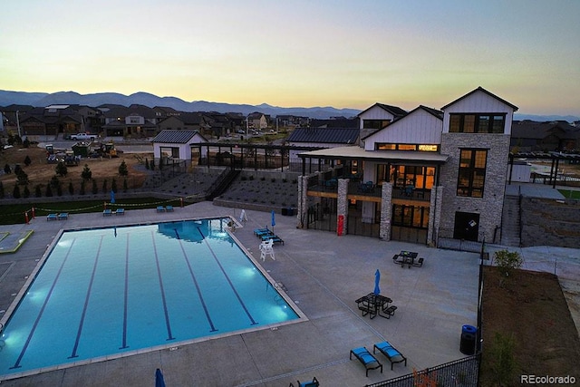 pool at dusk with a patio area, fence, a community pool, and a mountain view