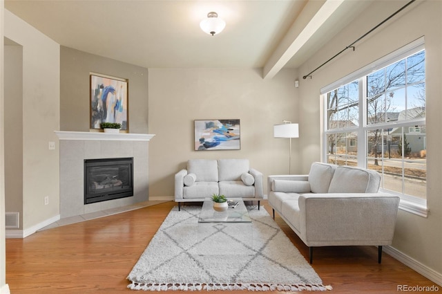 living room with baseboards, a tiled fireplace, visible vents, and wood finished floors