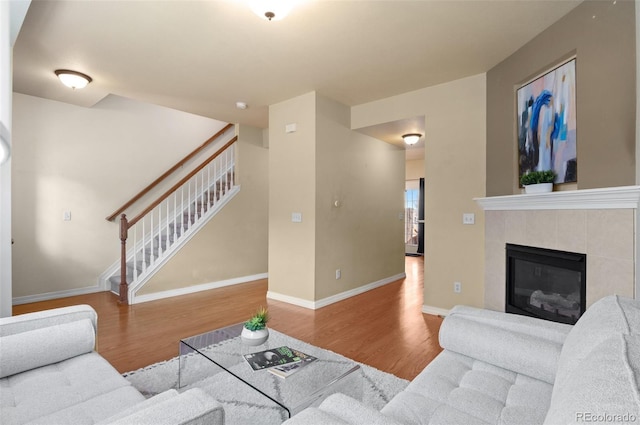 living area featuring a tile fireplace, stairway, baseboards, and wood finished floors