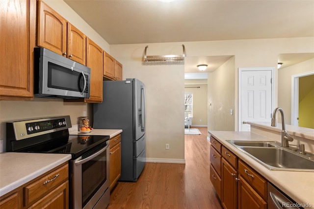 kitchen featuring stainless steel appliances, wood finished floors, a sink, light countertops, and brown cabinetry