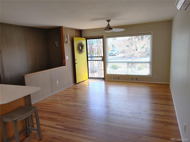 empty room featuring wood finished floors, visible vents, ceiling fan, and a wall mounted AC