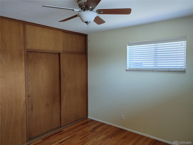 unfurnished bedroom with a closet, wood finished floors, a ceiling fan, and baseboards