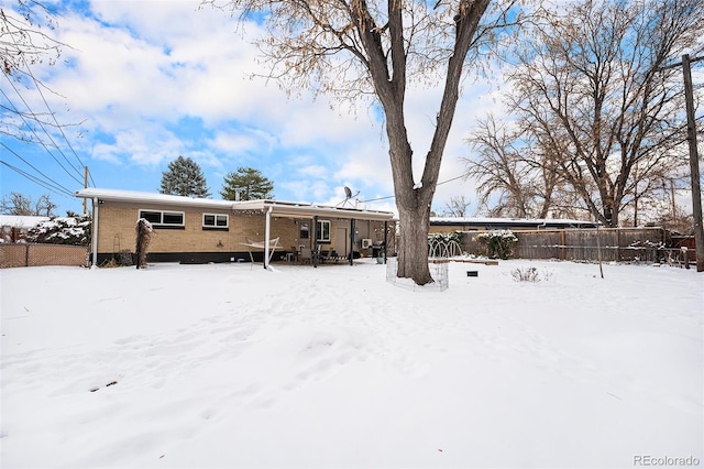 snow covered back of property with brick siding and fence