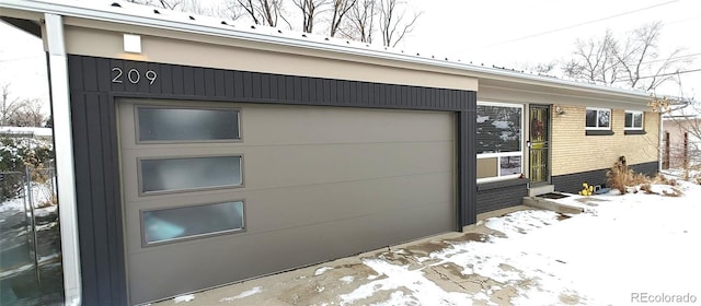 snow covered property featuring a garage and brick siding