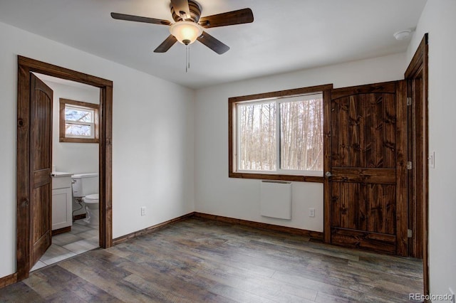 unfurnished bedroom featuring ensuite bathroom, wood finished floors, a ceiling fan, baseboards, and radiator