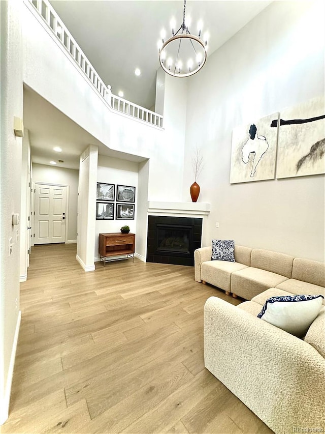 12743 W Bowles Pl, Littleton, CO 80127 - living area with a chandelier, light wood-type flooring, a towering ceiling, baseboards, and a glass covered fireplace