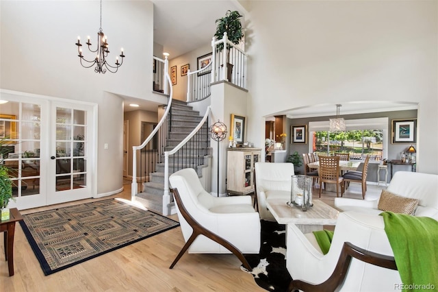 living room featuring an inviting chandelier, a towering ceiling, light hardwood / wood-style flooring, and french doors