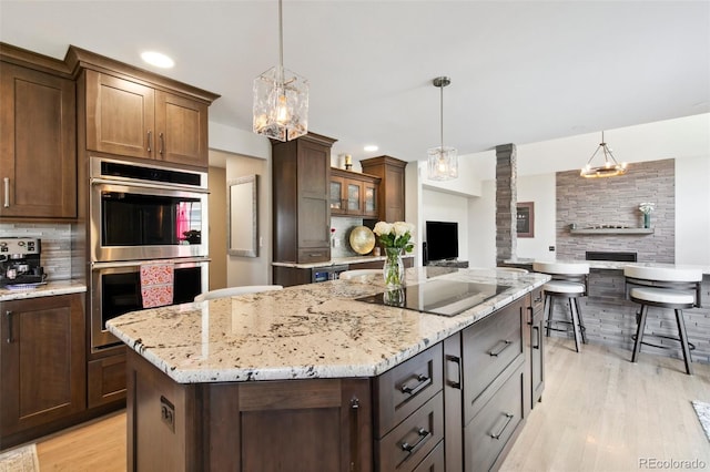 kitchen with dark brown cabinetry, hanging light fixtures, stainless steel double oven, black electric stovetop, and decorative backsplash