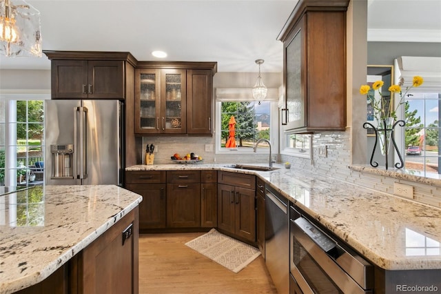 kitchen with hanging light fixtures, stainless steel appliances, sink, and light stone countertops