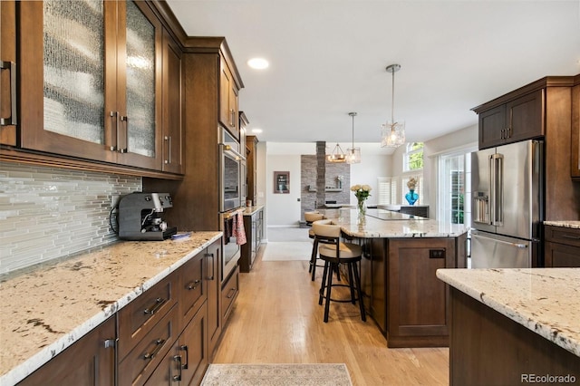 kitchen with high quality fridge, tasteful backsplash, hanging light fixtures, light hardwood / wood-style floors, and light stone countertops