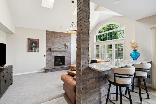 bar featuring a stone fireplace, high vaulted ceiling, decorative columns, light carpet, and decorative light fixtures