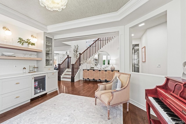 bar with dark wood-style flooring, crown molding, a dry bar, stairway, and beverage cooler