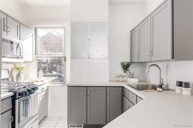 kitchen with a sink, appliances with stainless steel finishes, gray cabinetry, and light countertops