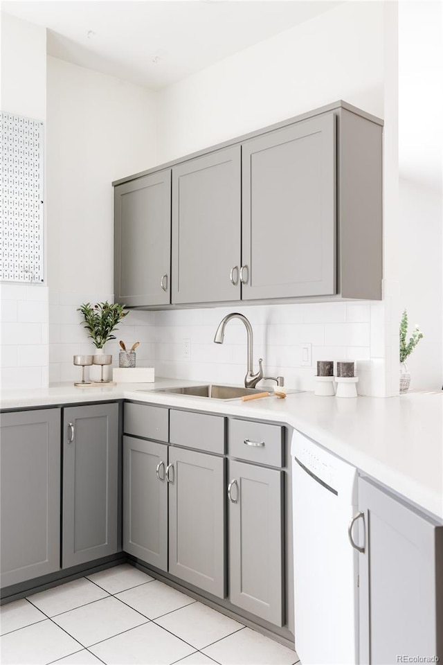 kitchen with gray cabinetry, a sink, tasteful backsplash, white dishwasher, and light countertops