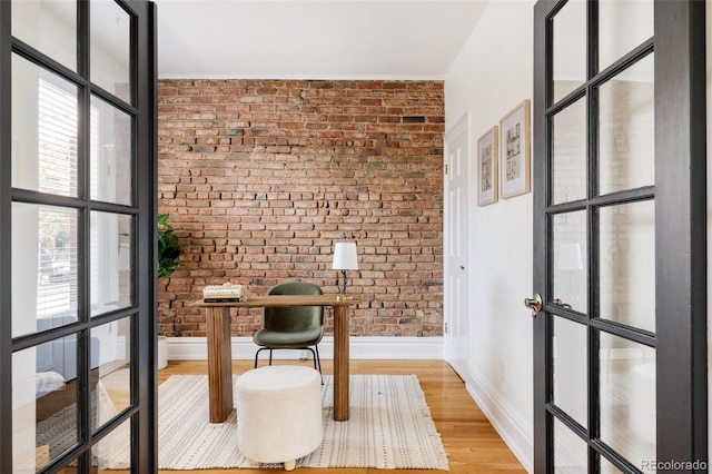 office area with brick wall, baseboards, and light wood finished floors