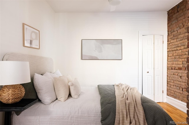 bedroom featuring wood finished floors, a closet, baseboards, and brick wall