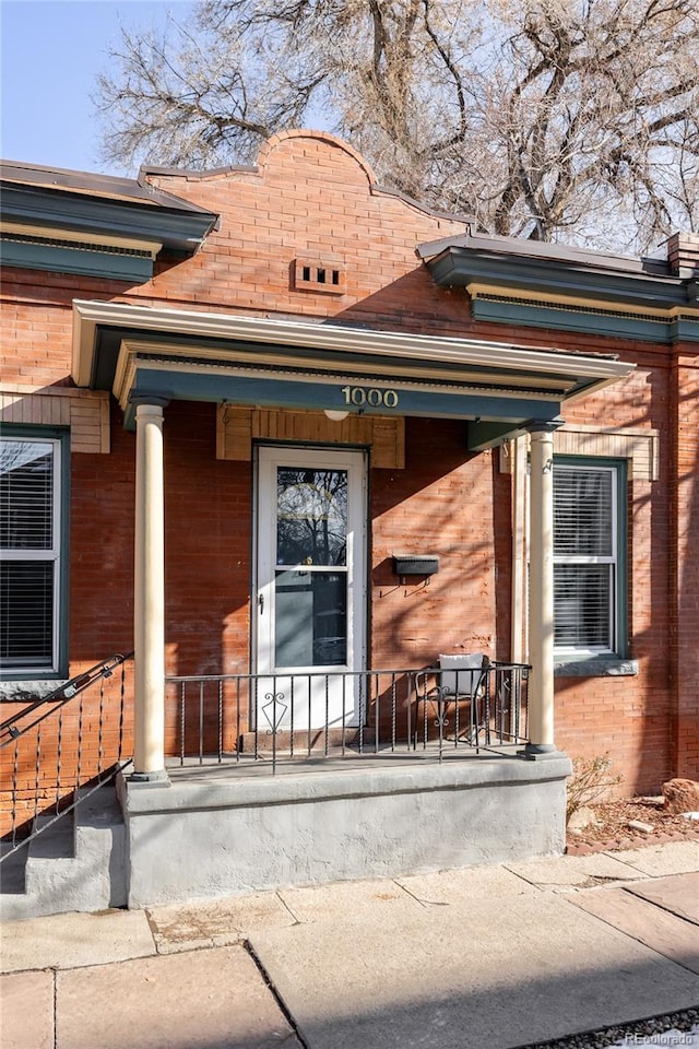 view of exterior entry featuring brick siding and covered porch