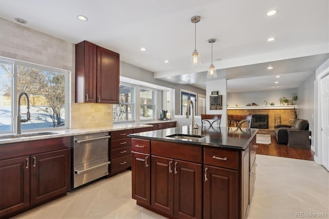 kitchen with hanging light fixtures, an island with sink, a brick fireplace, and sink