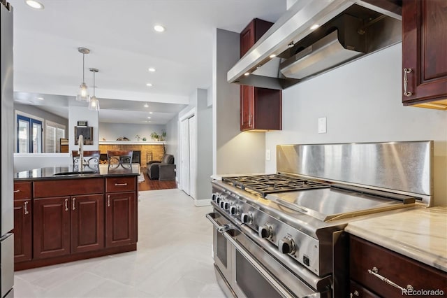 kitchen with wall chimney range hood, sink, double oven range, hanging light fixtures, and light stone countertops