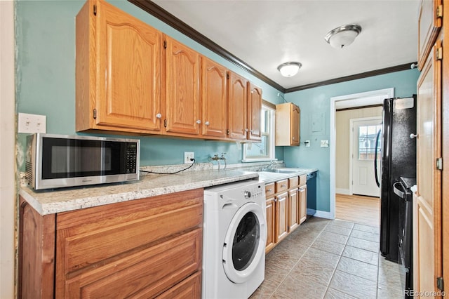 kitchen with crown molding, a sink, black appliances, washer / dryer, and baseboards