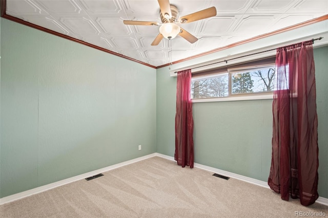 empty room featuring carpet floors, visible vents, a ceiling fan, baseboards, and an ornate ceiling