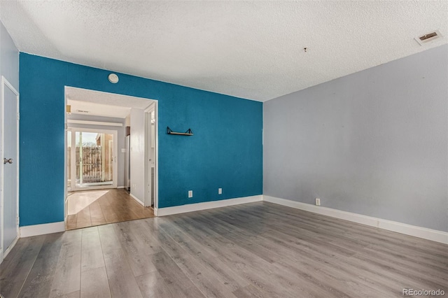 spare room featuring baseboards, wood finished floors, visible vents, and a textured ceiling