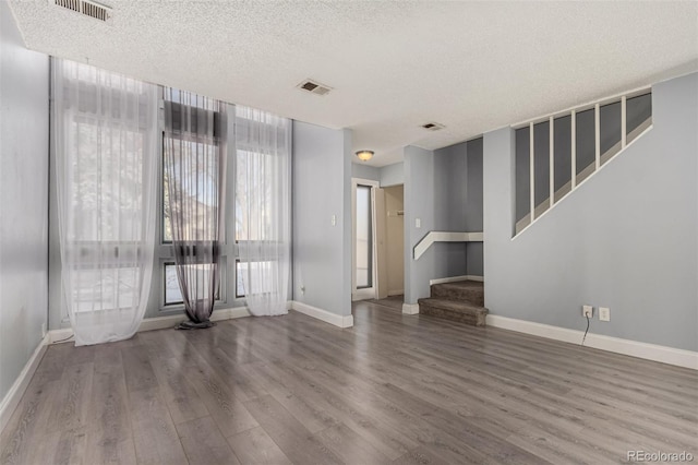 empty room with visible vents, baseboards, wood finished floors, and stairs