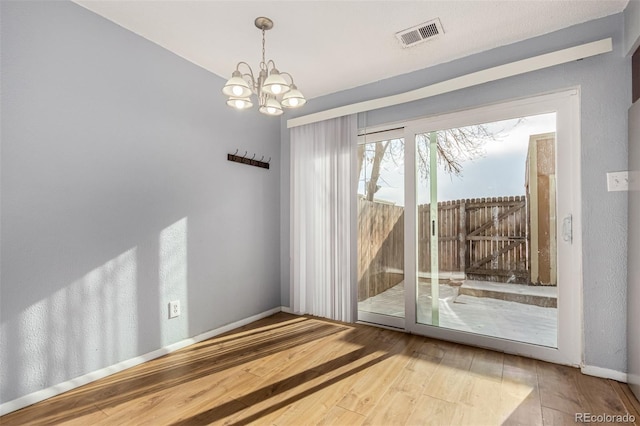 empty room featuring a notable chandelier, visible vents, baseboards, and wood finished floors