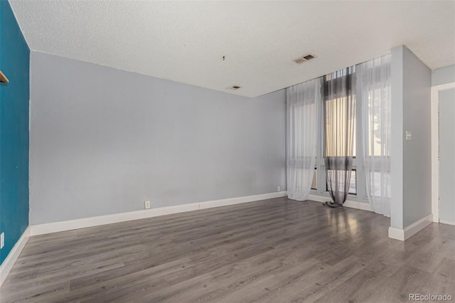 empty room with visible vents, a textured ceiling, baseboards, and wood finished floors