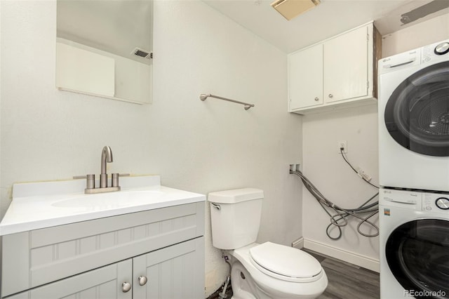 bathroom featuring visible vents, stacked washer and dryer, toilet, wood finished floors, and baseboards