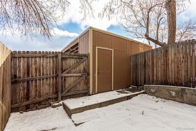 snow covered structure featuring a gate, an outdoor structure, a fenced backyard, and a shed