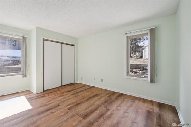unfurnished bedroom featuring a closet, a textured ceiling, wood finished floors, and baseboards