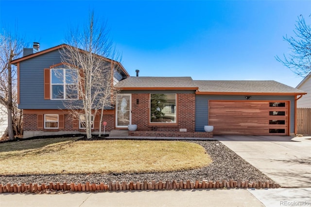 split level home featuring a front yard, concrete driveway, brick siding, and an attached garage