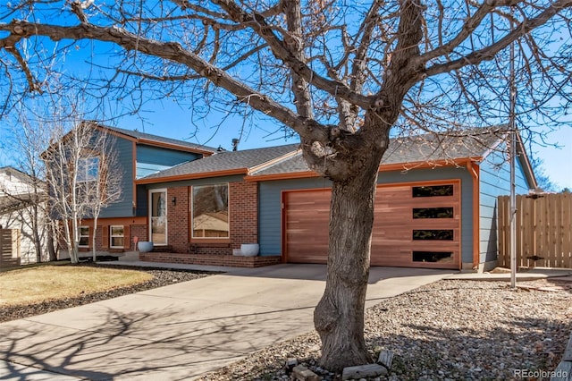 split level home with an attached garage, brick siding, fence, driveway, and roof with shingles