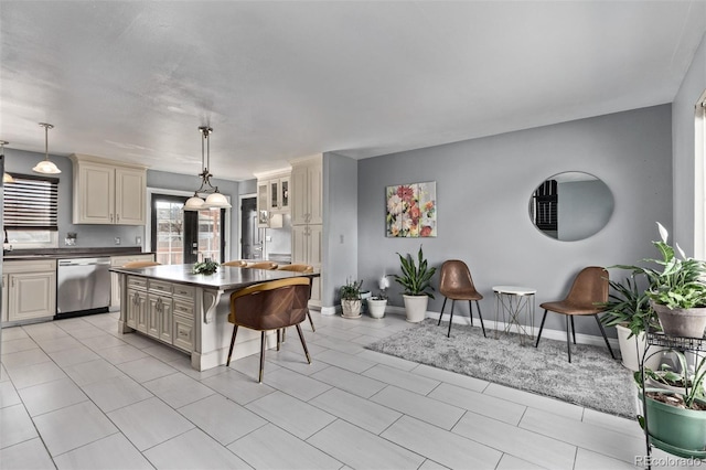 kitchen featuring a breakfast bar, a center island, cream cabinetry, dark countertops, and stainless steel dishwasher