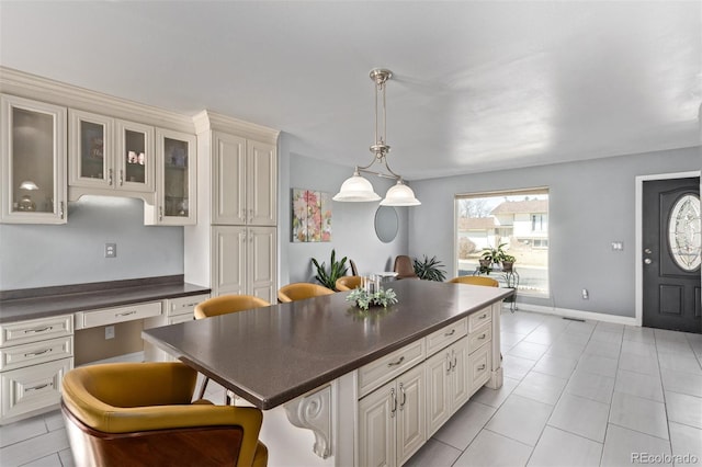 kitchen featuring dark countertops, hanging light fixtures, glass insert cabinets, built in study area, and a kitchen island