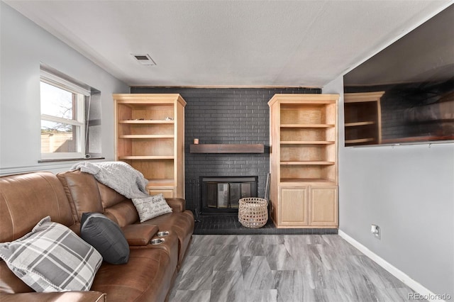 living room with a textured ceiling, a fireplace, wood finished floors, visible vents, and baseboards