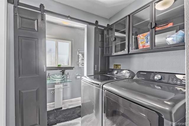 clothes washing area with cabinet space, a barn door, a sink, washer and dryer, and baseboards