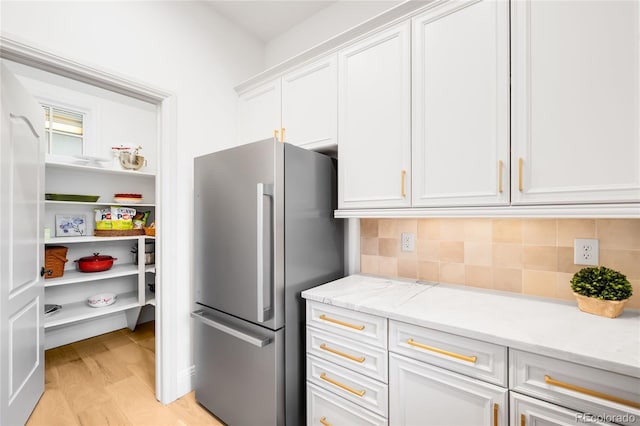 kitchen featuring freestanding refrigerator, white cabinetry, decorative backsplash, and light wood-style flooring