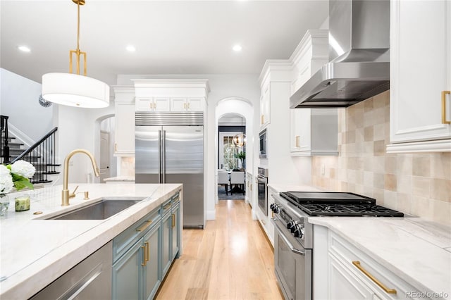 1164 S High St, Denver, CO 80210 - kitchen with wall chimney range hood, built in appliances, arched walkways, light wood-style floors, and white cabinets