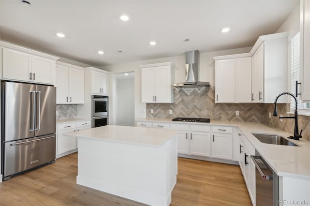 kitchen featuring a sink, appliances with stainless steel finishes, wall chimney exhaust hood, light wood-type flooring, and a center island