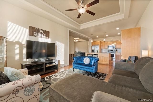 living room featuring hardwood / wood-style flooring, ceiling fan, and a raised ceiling