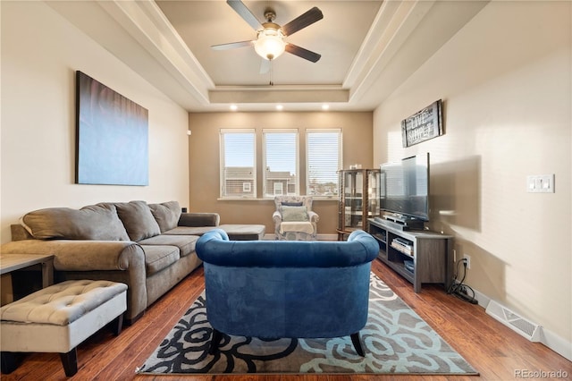 living room with hardwood / wood-style flooring, ceiling fan, and a raised ceiling