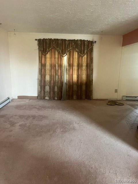 unfurnished room with a baseboard heating unit, carpet floors, and a textured ceiling